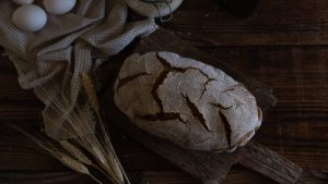 Artistic shot of homemade rustic bread with eggs and wheat on wooden table.