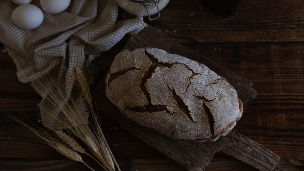 Artistic shot of homemade rustic bread with eggs and wheat on wooden table.